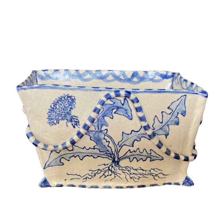ceramic square shaped bowl, cream colored with royal blue detailing. the top and bottom edges of the bowl are lined with blue stripes and there is a painting of a dandelion in light blue with a few spindly leaves. there is a raised striped coil that snakes around the bowl, creating a wavy effect.