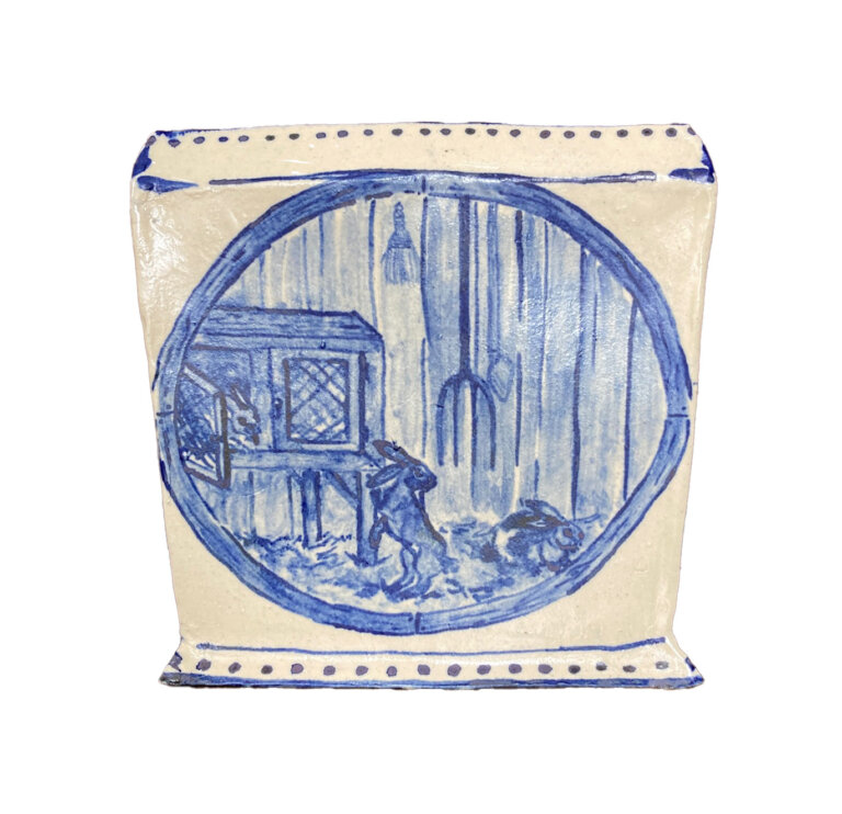 ceramic square shaped bowl, cream colored with royal blue detailing. on the front of the bowl is a circle frame painted with a small scene of three rabbits with a rabbit hutch. the hutch stands in hay against a wooden fence, on which hangs a pitchfork and a small brush.