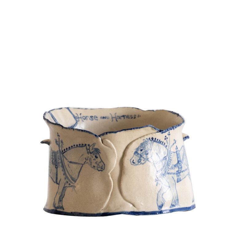 ceramic bowl with a flat bottom, cream colored with royal blue detailing. there are two clydesdale horses in blue facing each other wearing heavy harnesses. the inscription on the inside of the bowl reads "Horse and Harness"