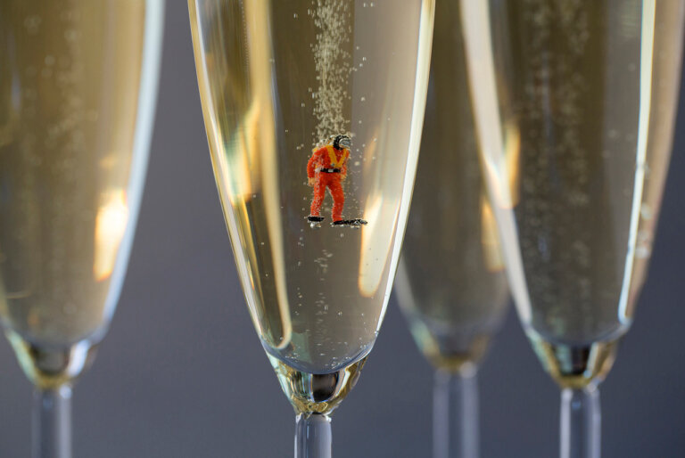 a creative photo where a tiny scuba diver is posed in a champagne glass with bubbles rising from him and from the bottom of the glass. there are three other glasses in the background.