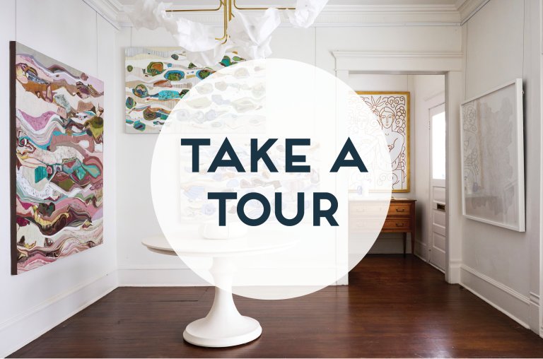 a photo of the interior of an art gallery with artwork from chase langford, stephanie strange, and shelley hesse. there is a white table with a bowl in the center of the room. overlaid on the photo is a graphic of a transparent white circle with the words "take a tour" printed in navy sans serif capital letters