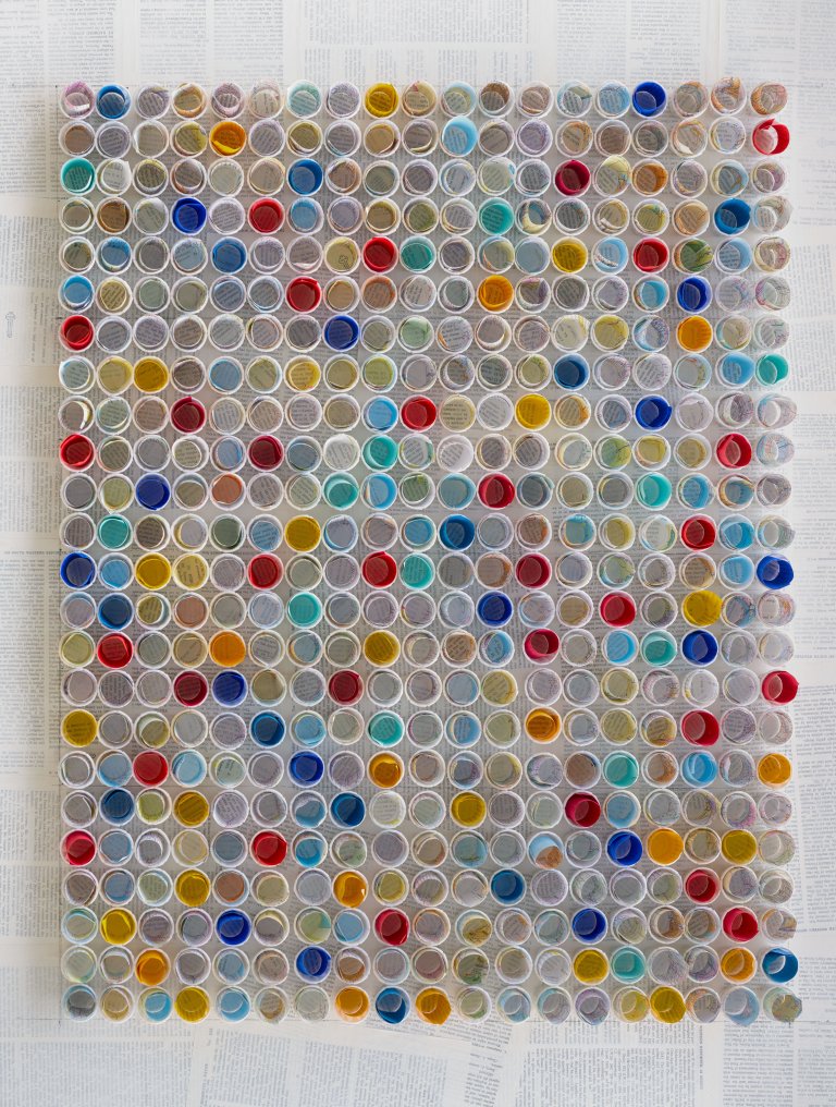 a straight on view of a 3d sculpture piece of small white paper cups arranged in rows, each holding a small roll of colored paper in shades of orange, cobalt, lemon yellow, kelly green, mint, pale aqua, cherry red, slate, mauve, lavender, peach, bubblegum pink, terra cotta, and ultramarine blue