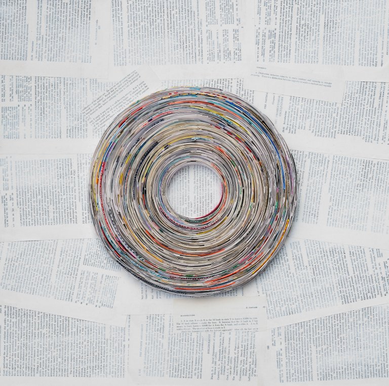 an abstract collaged piece that resembles a vinyl record. there are small pieces of paper swirled in a circle shape. the background is collaged with book pages and has a thin layer of white paint over top that creates a faded look