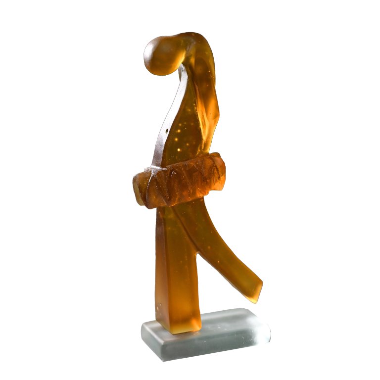 a hand cast glass sculpture in amber glass with a clear base. the dancer wears a powder puff tutu, standing with her weight on her front leg and her back leg extended and raised up slightly in a half arabesque. the figure's head is bowed forward, and her hands are clasped behind her back. the air and feeling communicated by this sculpture is similar to that of edgar degas' sculpture "the little dancer"