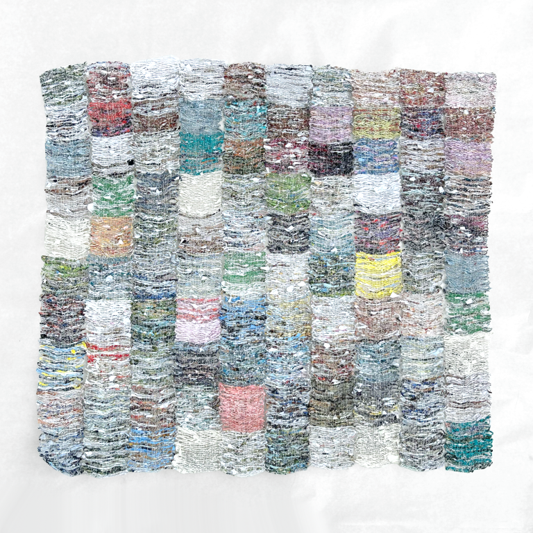 an abstract woven quilt-like art piece made of handspun paper. the paper is woven into small squares that are stitched together in 10 rows of 10 squares. the colors are muted, mostly white and gray with accents of peach, sky blue, sage, yellow, and lilac