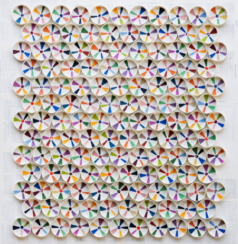 an abstract piece of art made up of circles arranged edge to edge in 13 horizontal rows of 11 and 10, alternating. the circles are made of white paper, and there is a colorful pinwheel stripe inside each one in shades of lime green, cobalt, vibrant orange, vermillion, magenta, lilac, mint green, tawny, peach, and many more. the background behind the shape is layered with law book pages that are whitewashed