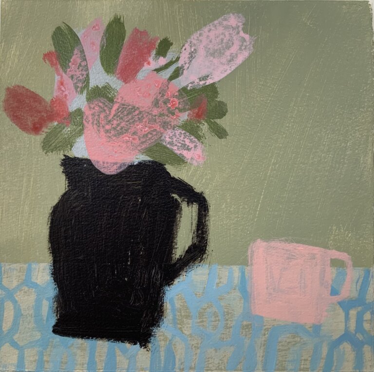 a simplified still life with a blue and cream patterned tablecloth on a table against a sage green wall. on the table is a black jug filled with pink flowers. there is a small pink mug on the table to the right of the jug