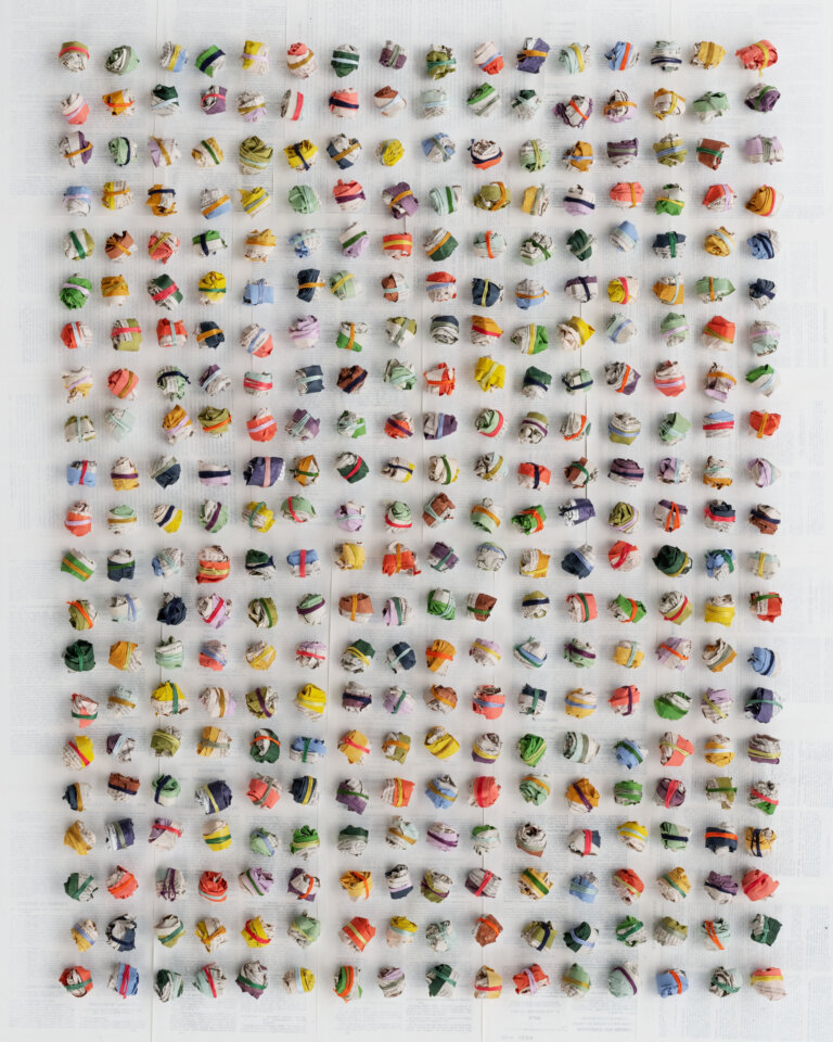 a collage of balled up pages from law books tied with multi colored threads and laid in a grid, 21 balls high by 16 balls wide